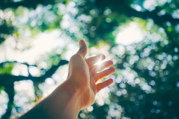 woman's hand reaching out for help and comfort from grief, green foliage background