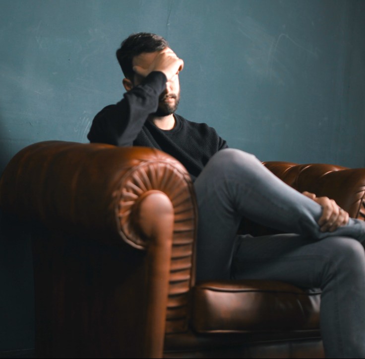 man alone on couch covering face, grieving alone